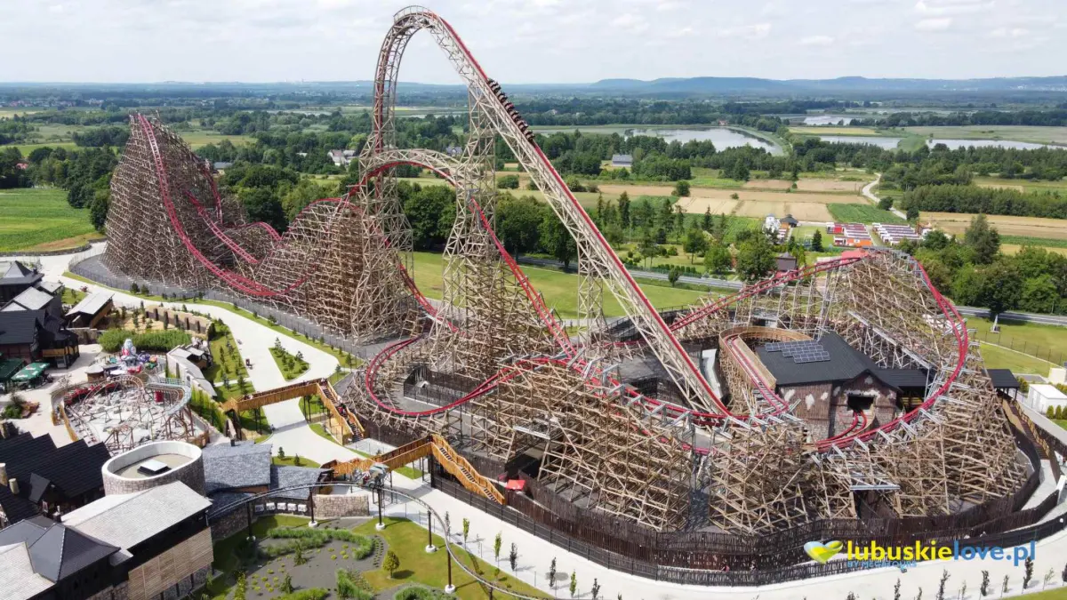 Widok na rollercoaster w Energylandii z zielonymi polami w tle.